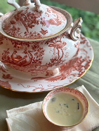 A bowl or white soup next to a red-and-white soup tureen